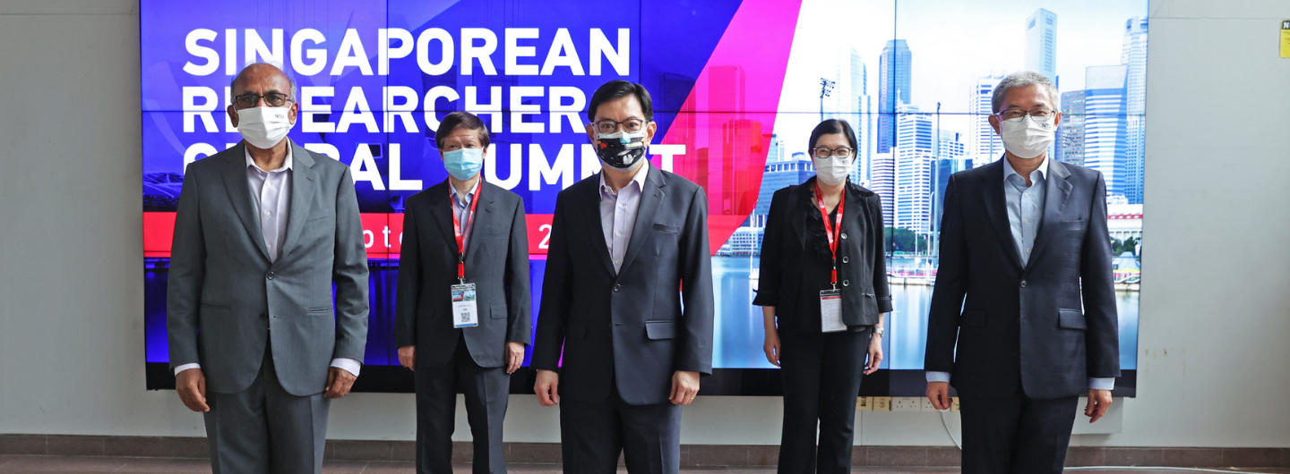Five people wearing suits and face masks stand before a "Singaporean Researcher Global Summit" banner.